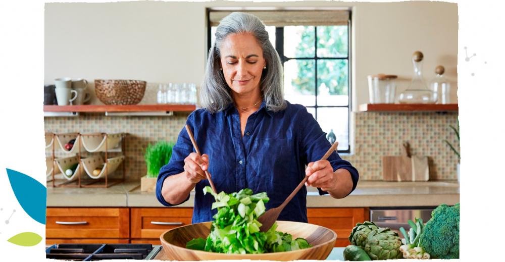Starsza kobieta w granatowej bluzce robiąca sałatkę.