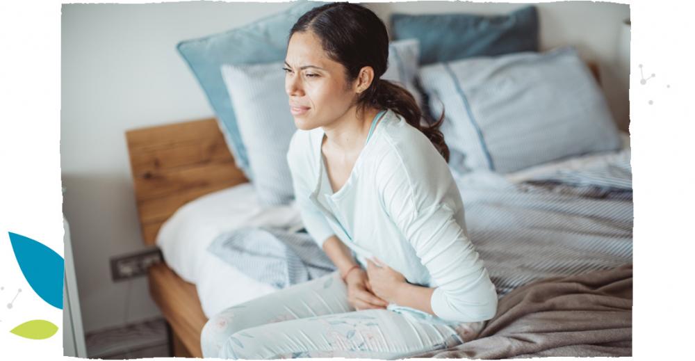 Kobieta siedząca na łóżku i trzymająca się za brzuch.