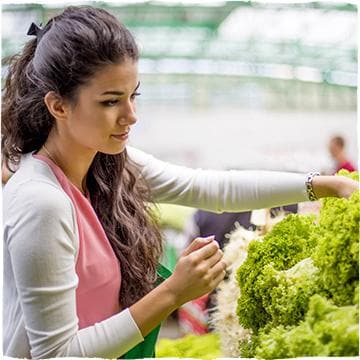 Young woman choosing from various kinds of lettuce while making groceries.