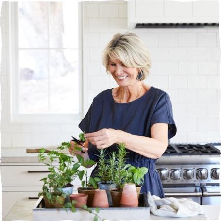 Starsza kobieta pielęgnuje zioła w swojej kuchni.
