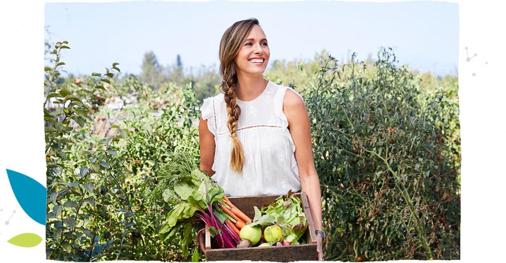 Młoda uśmiechnięta kobieta trzyma skrzynkę pełną warzyw.