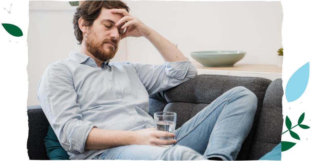 Mężczyzna siedzący na kanapie i trzymający szklankę z wodą.