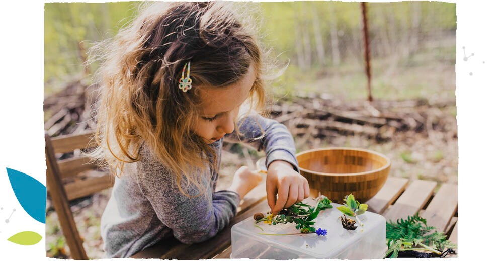 A little girl playing with leaves and flowers on a garden table.